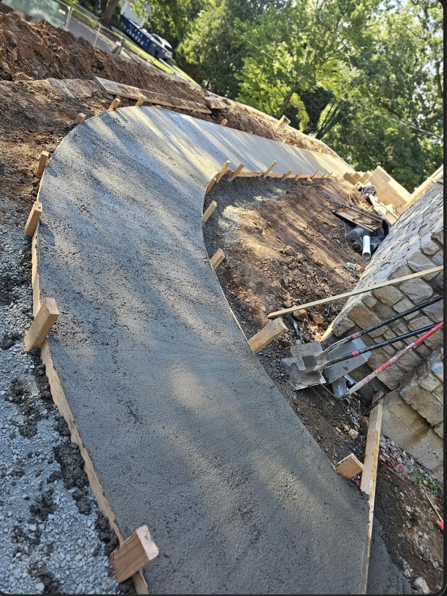 A curved concrete walkway poured next to a new stone wall
